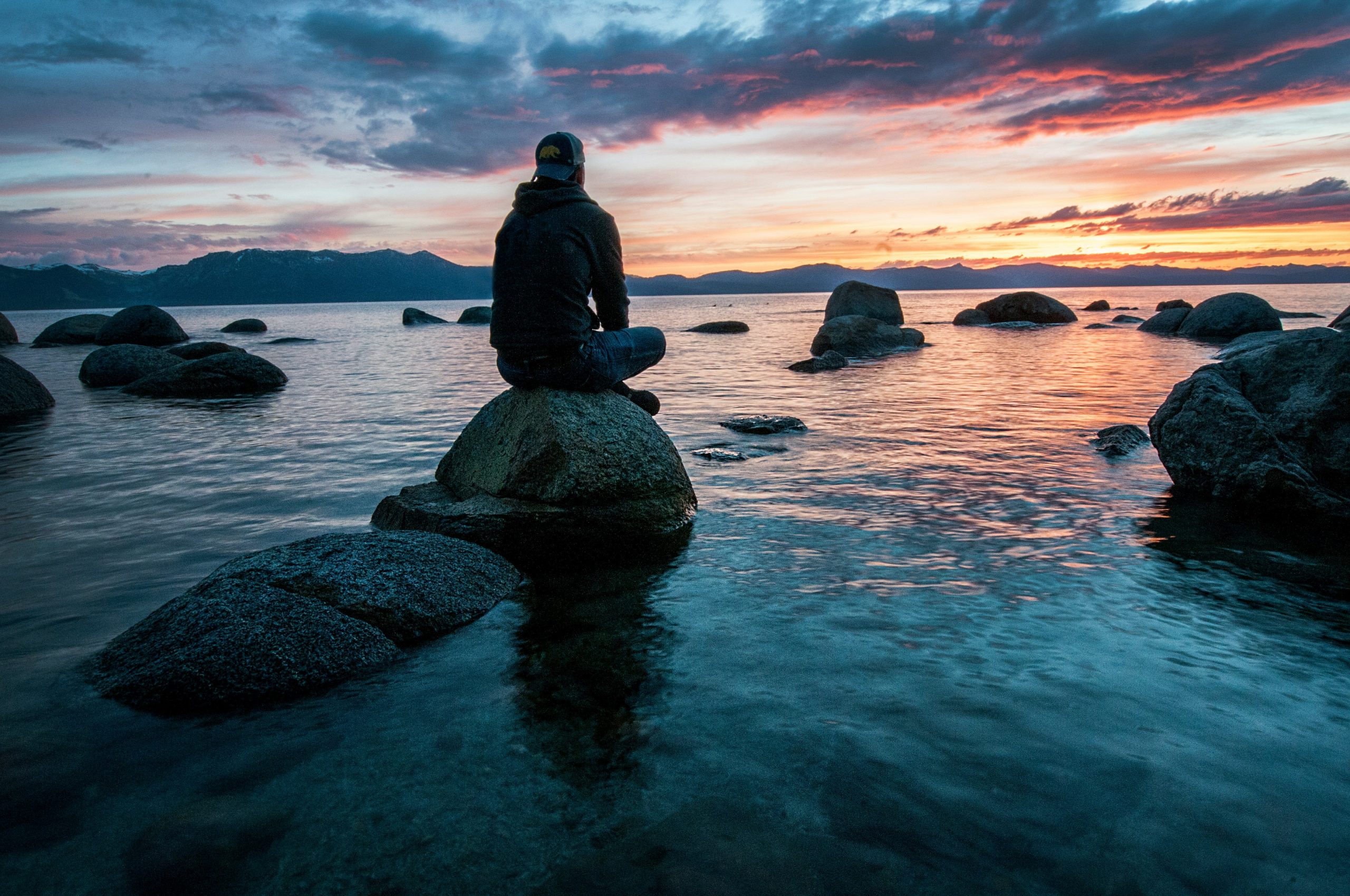 Person sitting on rock in the water watching the sunset.