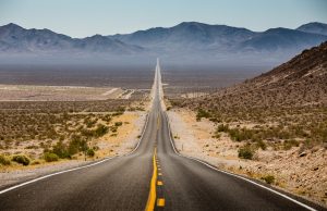 Classic panorama view of an endless straight road running through the barren scenery of the American Southwest with extreme heat haze on a beautiful sunny day with blue sky in summer