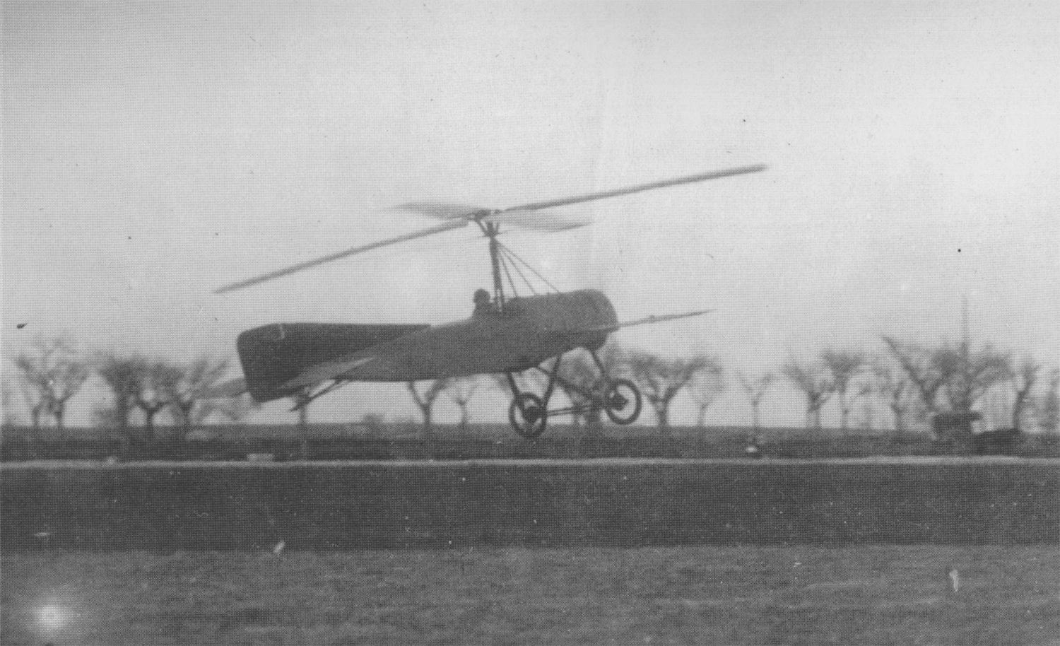 A grainy black and white photograph of an aircraft lifting off with one large rotating propeller above the pilot.