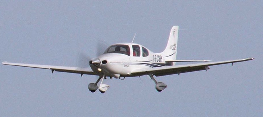 Photograph of a small white airplane with a nose propeller flying towards the camera on a hazy background.