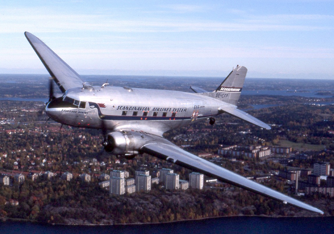 Photograph of a silver airplane flying over a city.