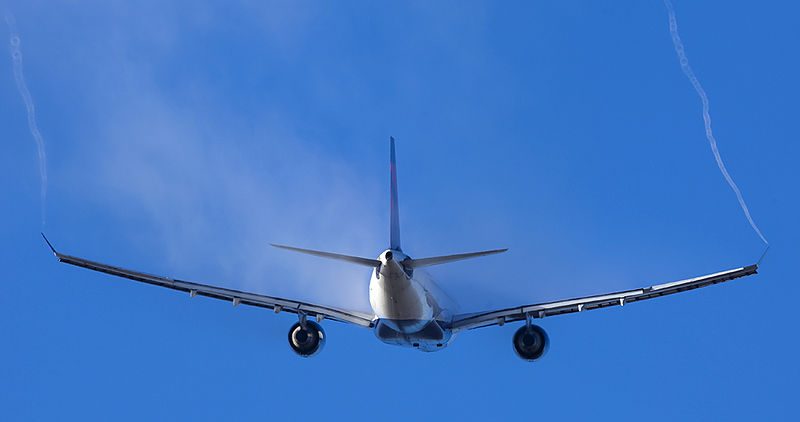 A Boeing A330 Aircraft flying away from the camera on a clear sky background. White water vapor is trailing off the wings and the winglet tips.