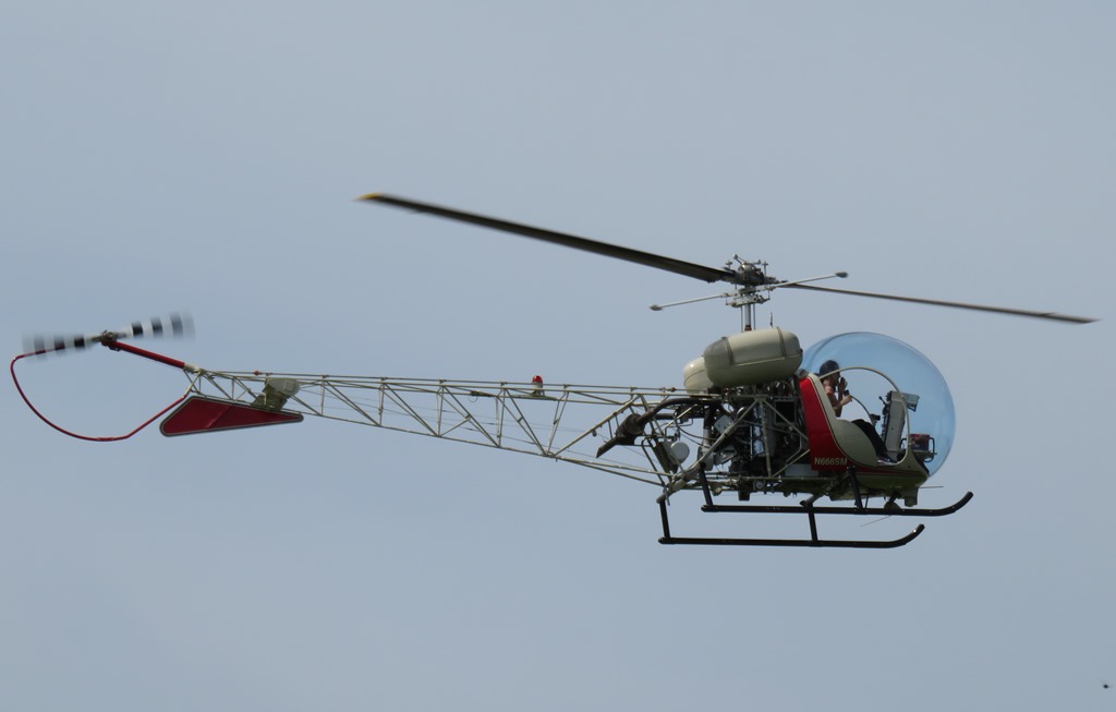 Photograph of a helicopter on a grey sky background. The helicopter has mostly visible framework and a clear bubble-style cockpit.