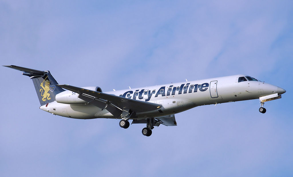Photograph of a white and blue jet airplane flying to the right on hazy blue background. The plane has a lion painted on the tail and City Airline on the fuselage.