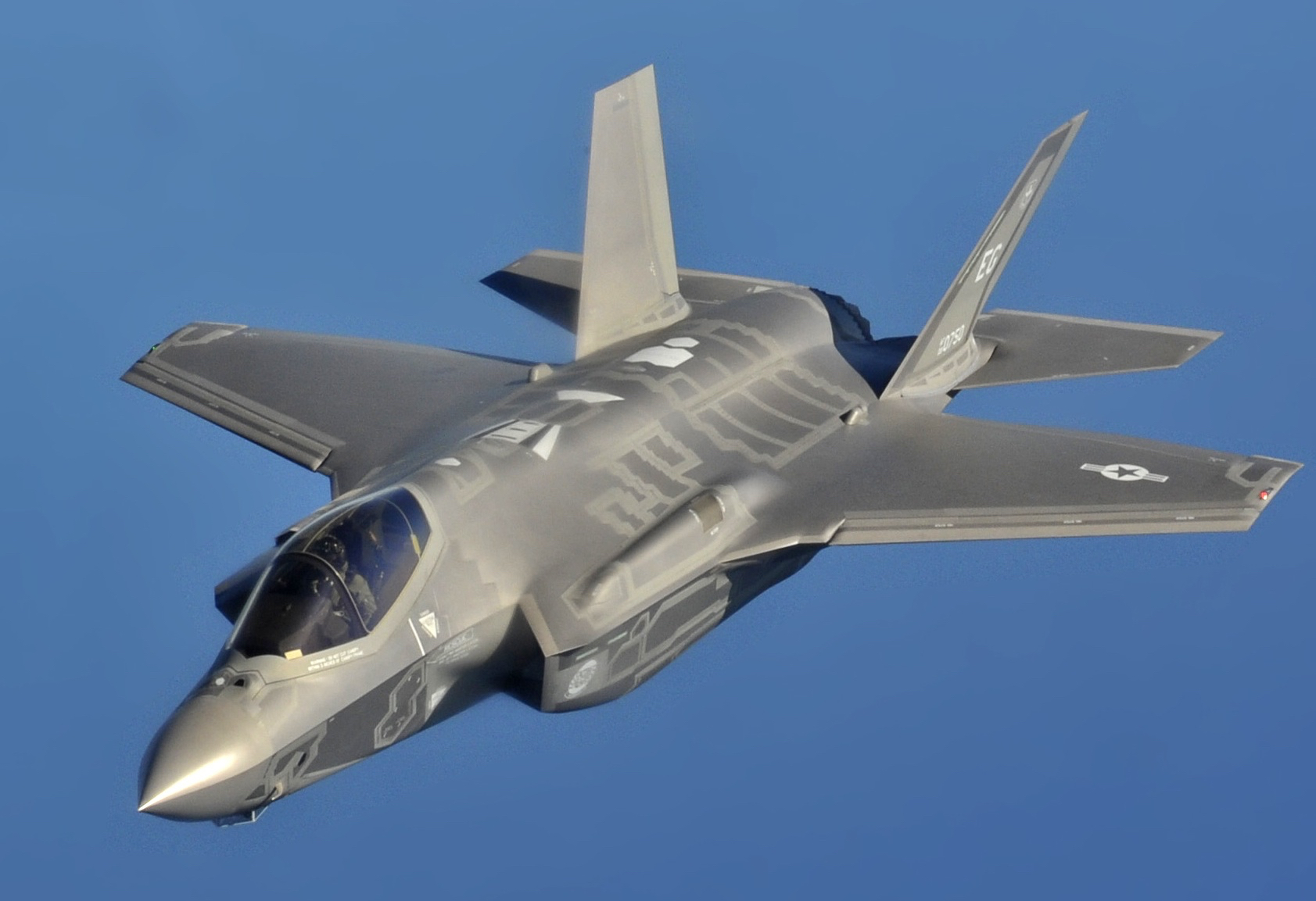 Photograph of a grey airplane on a blue sky background flying towards the lower left corner.